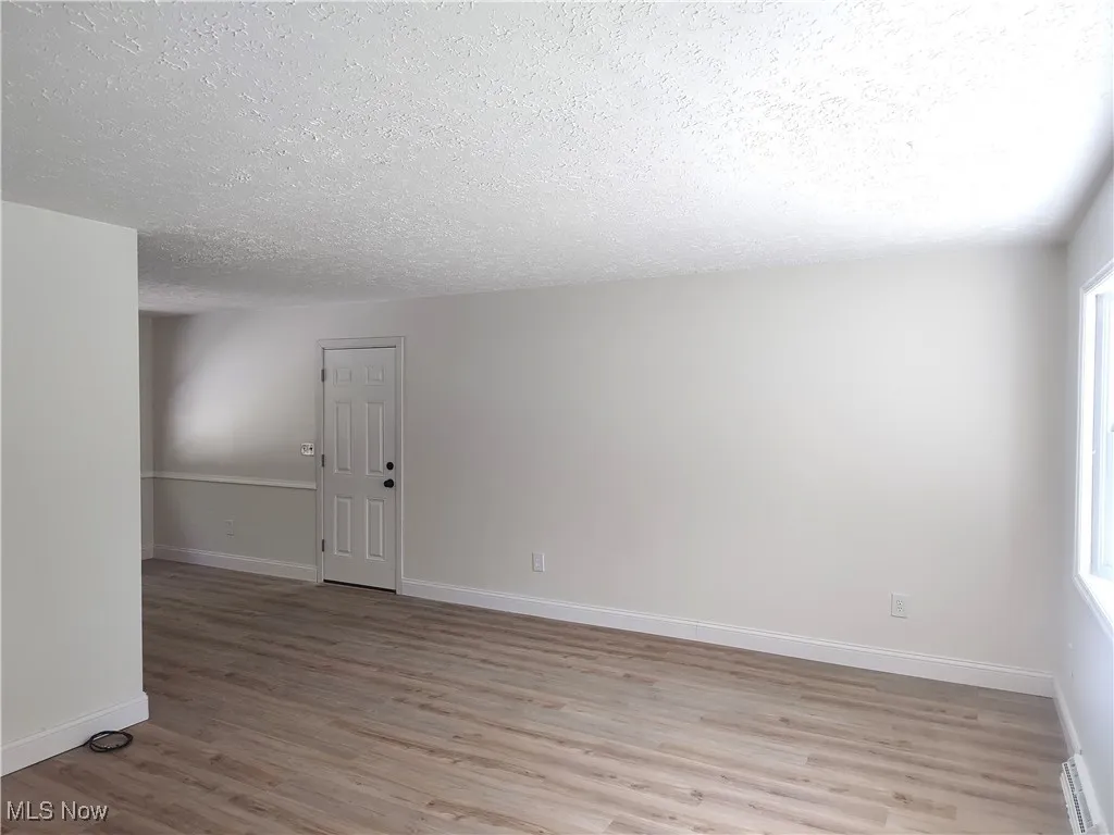 Spare room with light wood-style floors, a textured ceiling, healthy amount of natural light, and a baseboard heating unit