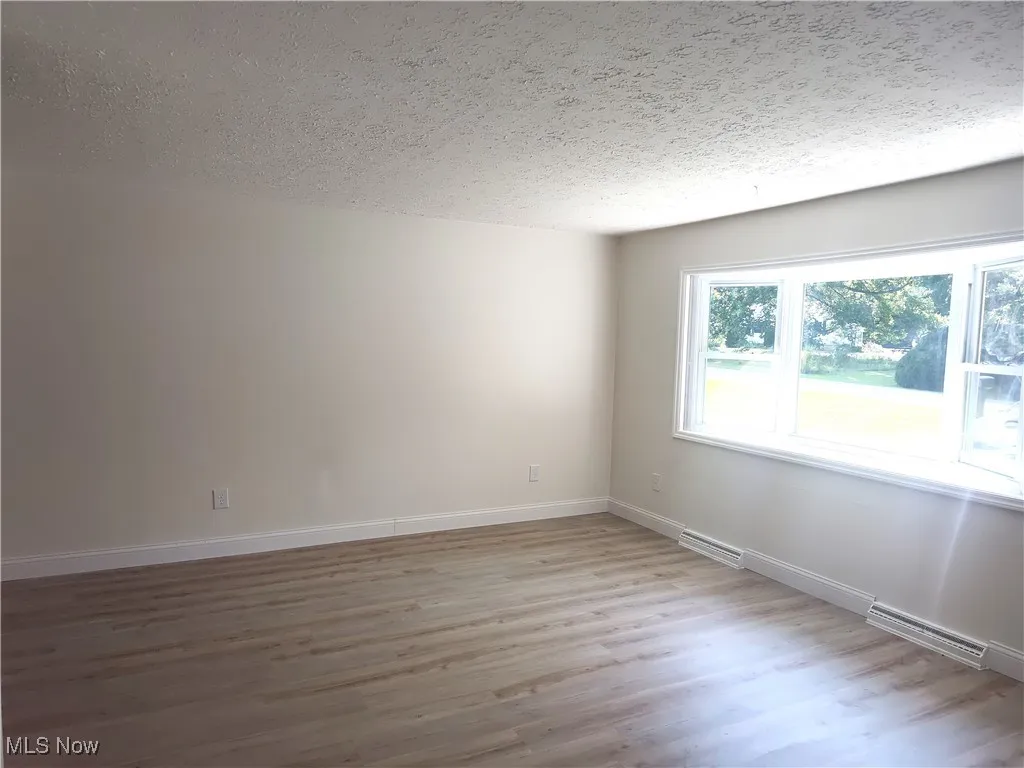 Empty room with light wood-style floors and a textured ceiling