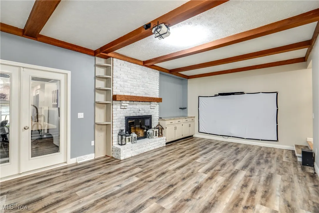 Unfurnished living room featuring beamed ceiling, light wood-style flooring, a fireplace, and a textured ceiling