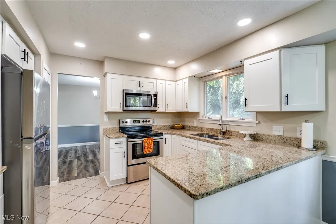 Kitchen featuring appliances with stainless steel finishes, light stone counters, light tile patterned floors, a peninsula, and white cabinets