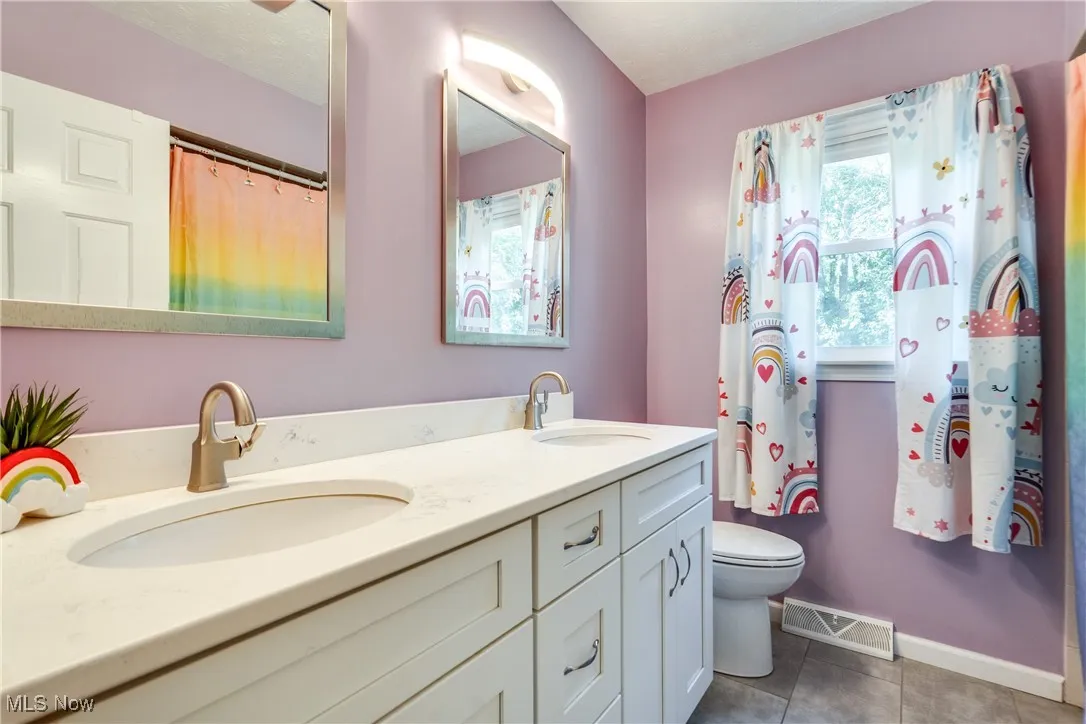 Full bath with plenty of natural light, double vanity, and dark tile patterned flooring