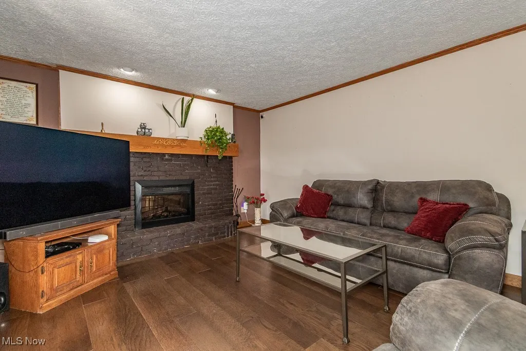 Family room featuring crown molding, dark wood-style flooring, a brick fireplace, and a textured ceiling