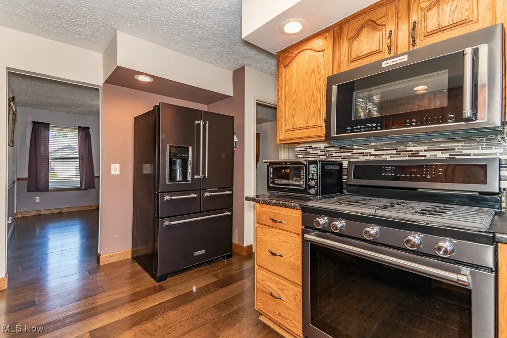 Kitchen view of appliances with stainless steel finishes, a textured ceiling, wood finished floors, brown cabinets, and tasteful backsplash