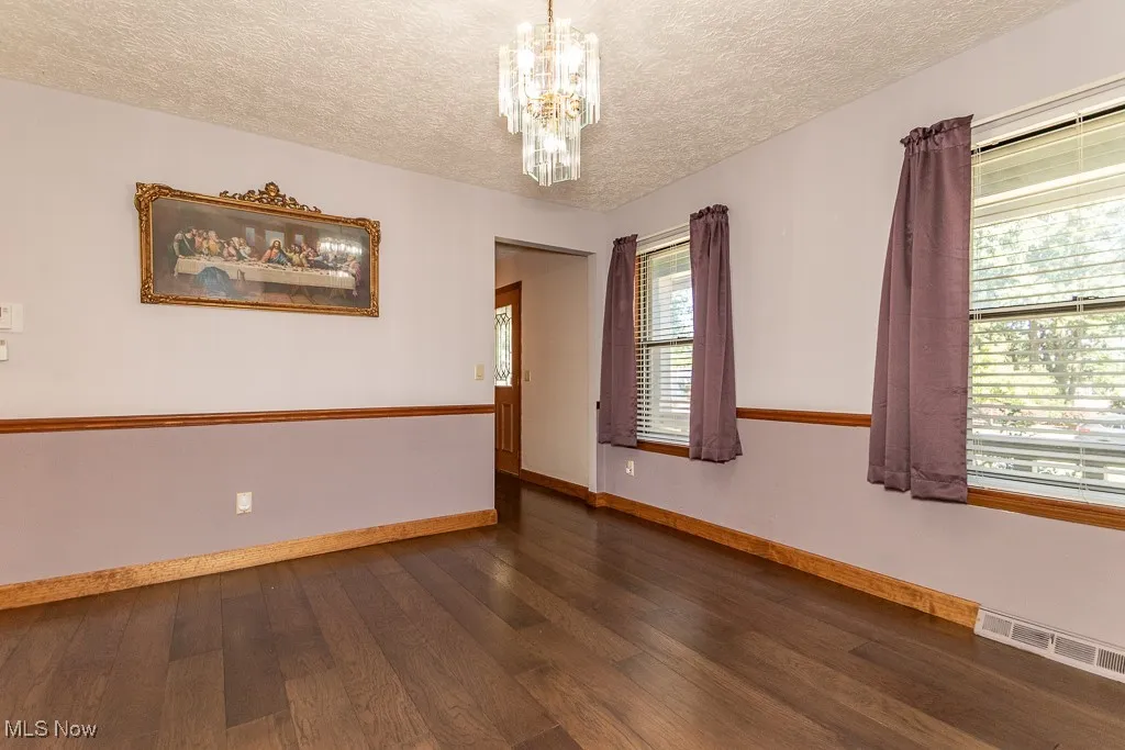Unfurnished dining room featuring dark wood-type flooring, and a chandelier