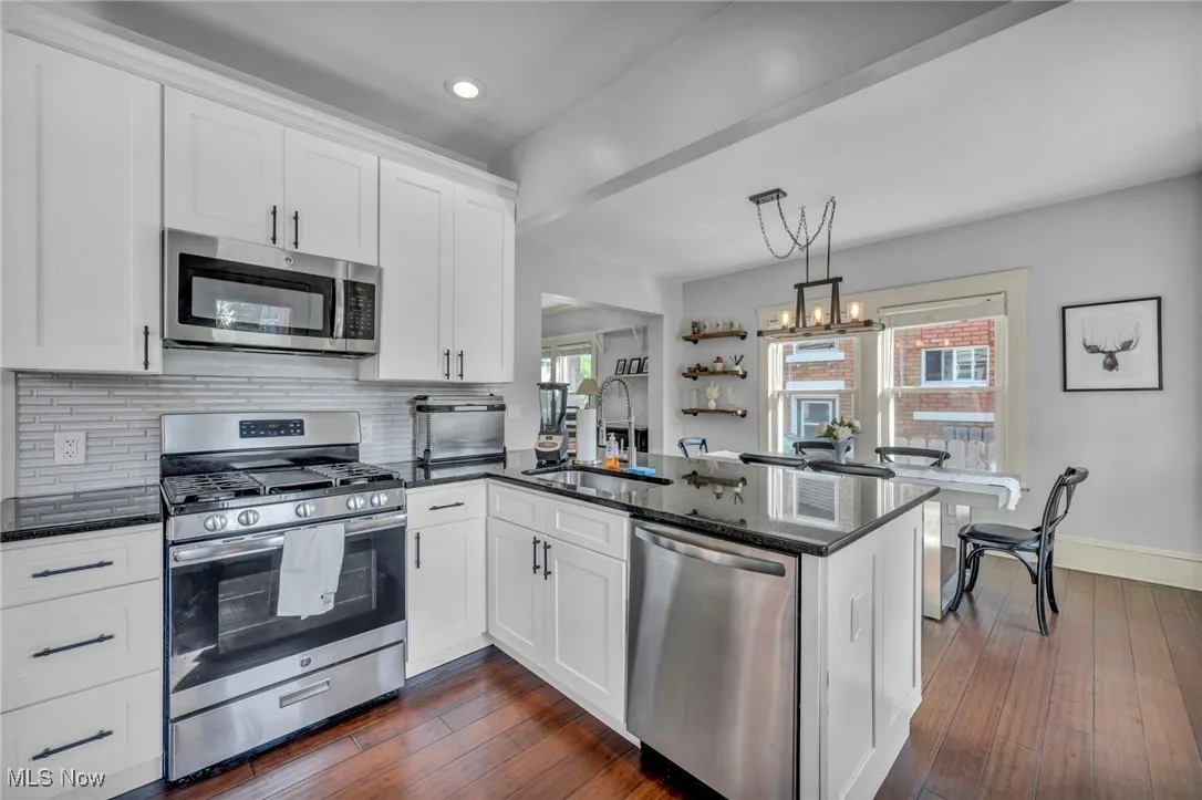 Kitchen with appliances with stainless steel finishes, white cabinetry, dark stone countertops, a peninsula, and dark wood-style flooring