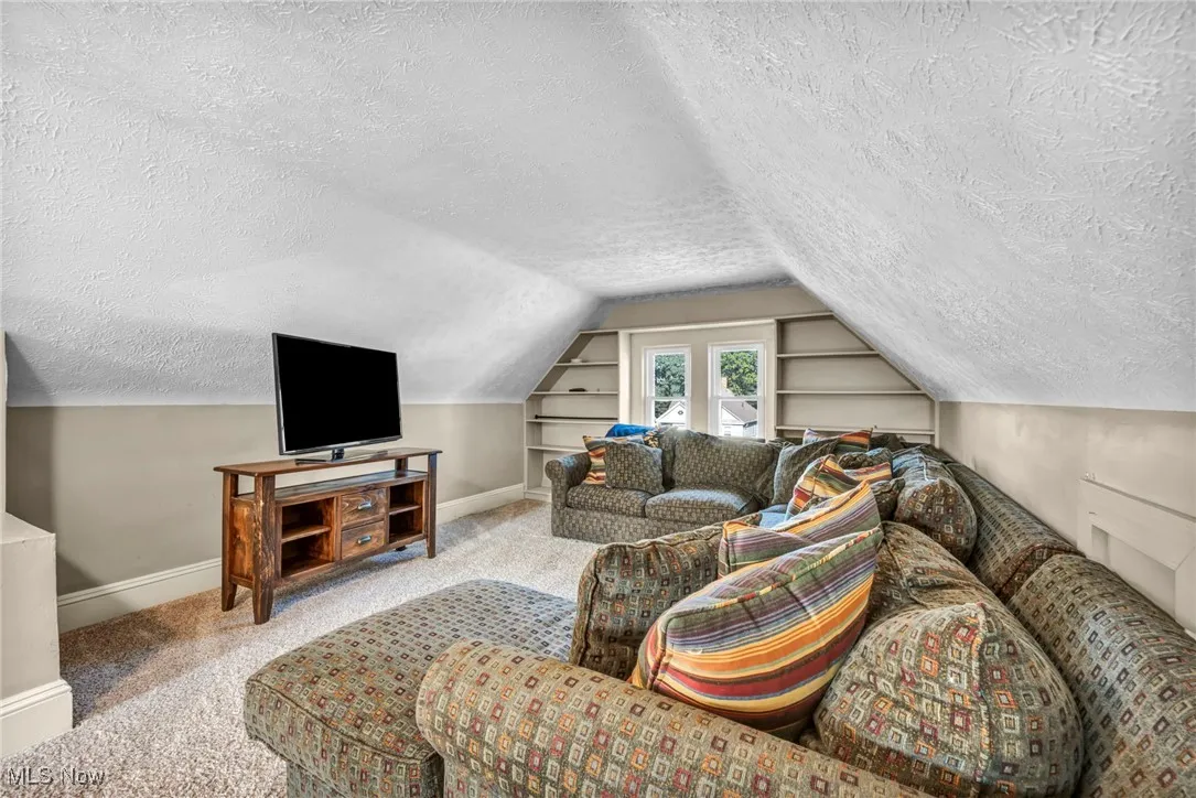 Carpeted living room featuring built in features, a textured ceiling, and vaulted ceiling