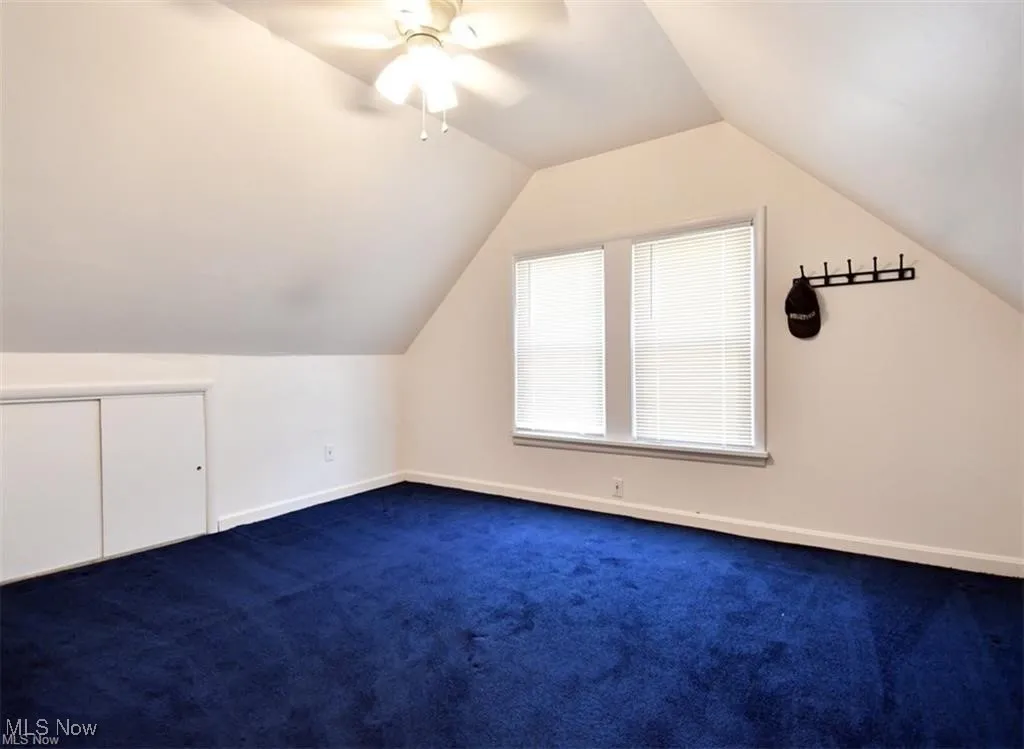 Additional living space featuring dark colored carpet, lofted ceiling, and a ceiling fan