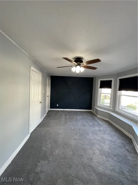 Unfurnished bedroom featuring dark carpet, a textured ceiling, and ceiling fan