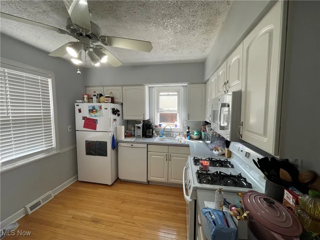Kitchen featuring white appliances, light wood-style floors, a textured ceiling, a ceiling fan, and white cabinetry