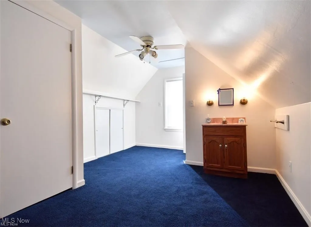 Additional living space with vaulted ceiling, dark carpet, and a ceiling fan