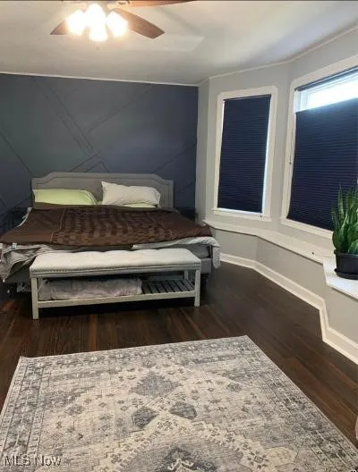 Bedroom featuring dark wood-style floors, ceiling fan, and a decorative wall