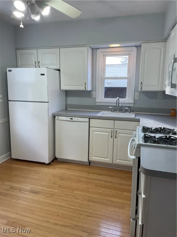 Kitchen with range, light wood-style floors, white cabinets, white dishwasher, and stainless steel microwave