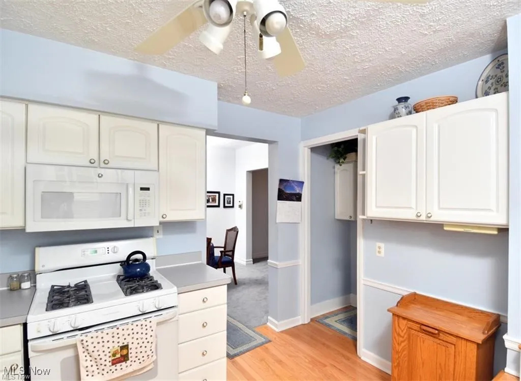 Kitchen featuring white appliances, light wood finished floors, a textured ceiling, light countertops, and ceiling fan