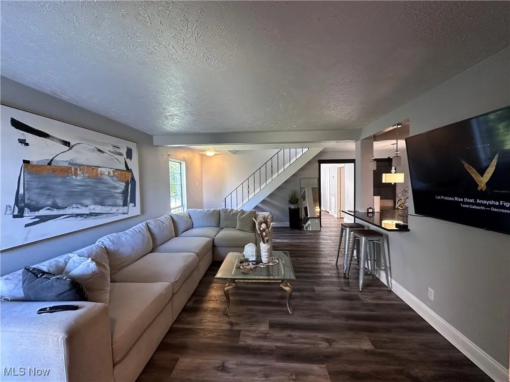 Living area featuring a textured ceiling, dark wood-style floors, and stairs