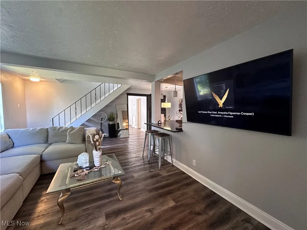 Living area with a textured ceiling, dark wood-type flooring, and stairway