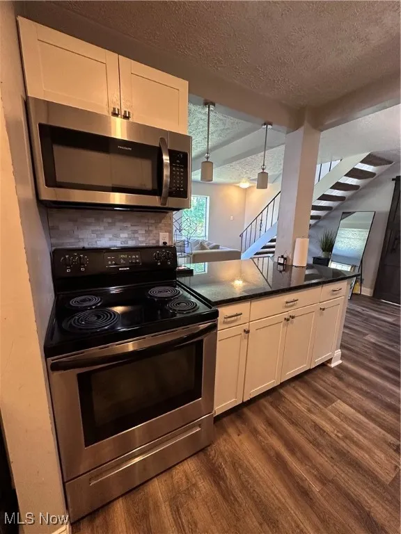 Kitchen featuring stainless steel stove, white cabinets, a textured ceiling, dark wood-style floors, and a peninsula