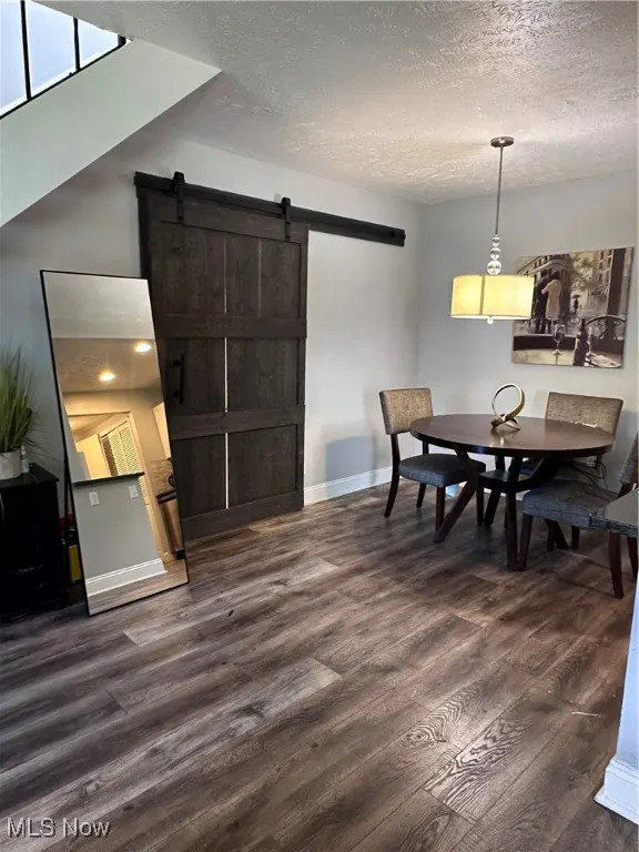 Dining room with a barn door, dark wood finished floors, and a textured ceiling