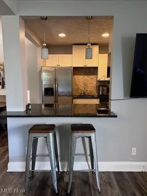 Kitchen with stainless steel refrigerator with ice dispenser, a breakfast bar, decorative backsplash, and pendant lighting