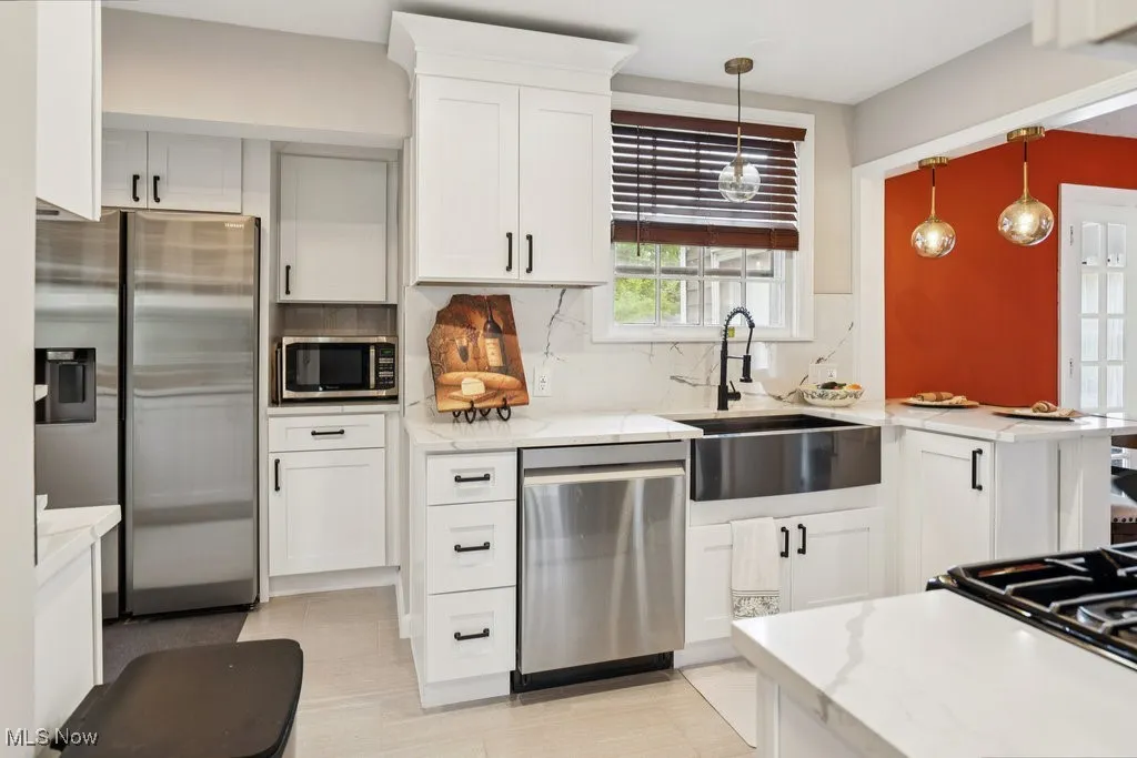 Kitchen featuring appliances with stainless steel finishes, backsplash, light stone countertops, and white cabinets