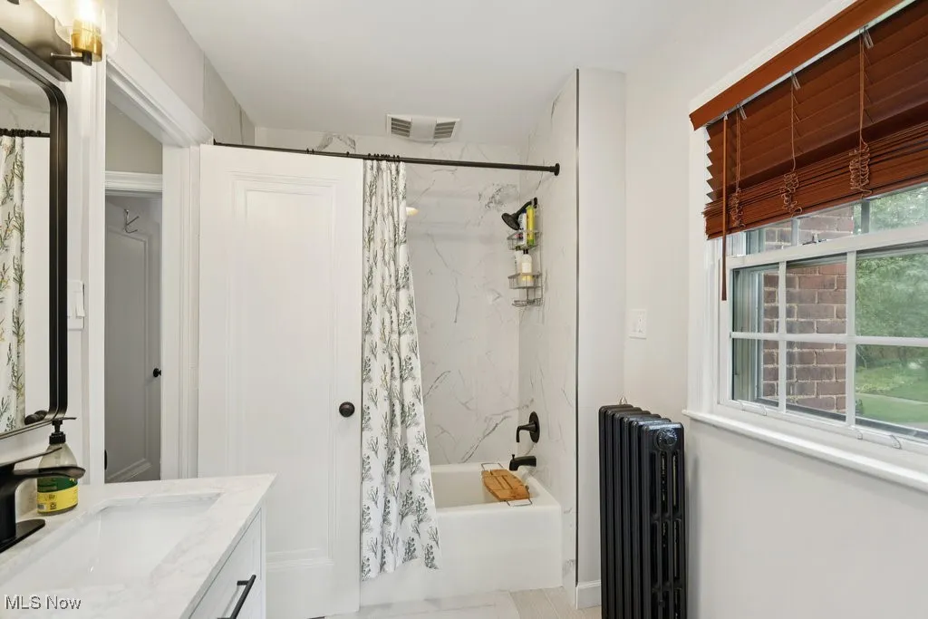 Bathroom featuring shower / bathtub combination with curtain, radiator heating unit, and vanity