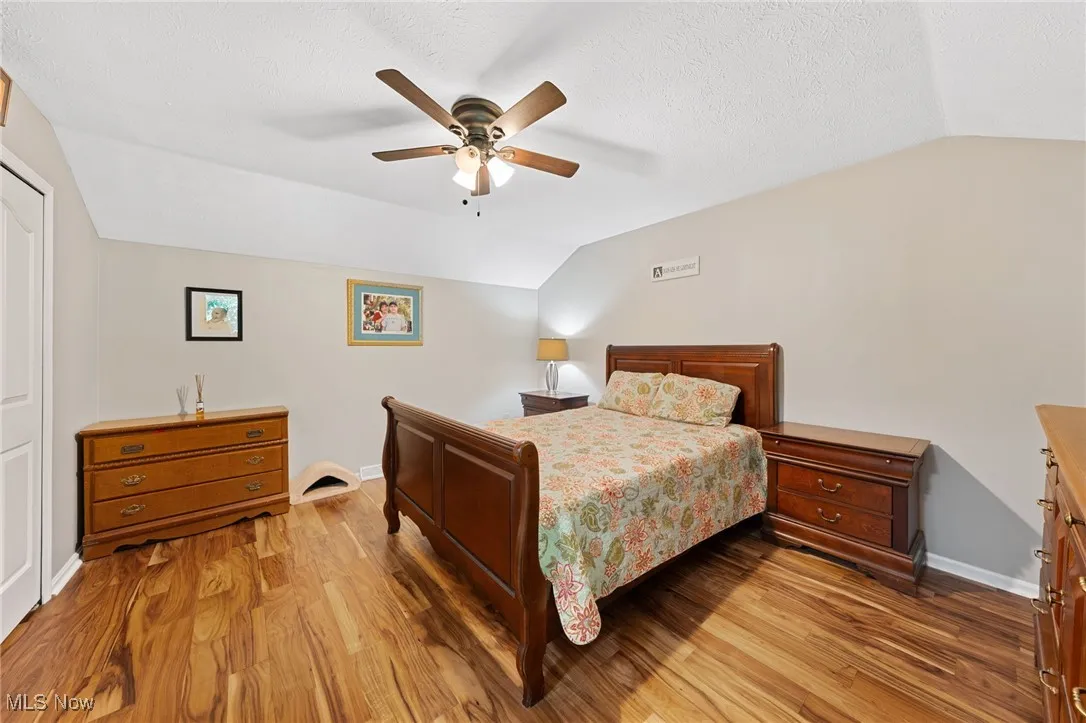 Bedroom featuring lofted ceiling, light wood finished floors, ceiling fan, a closet, and a textured ceiling