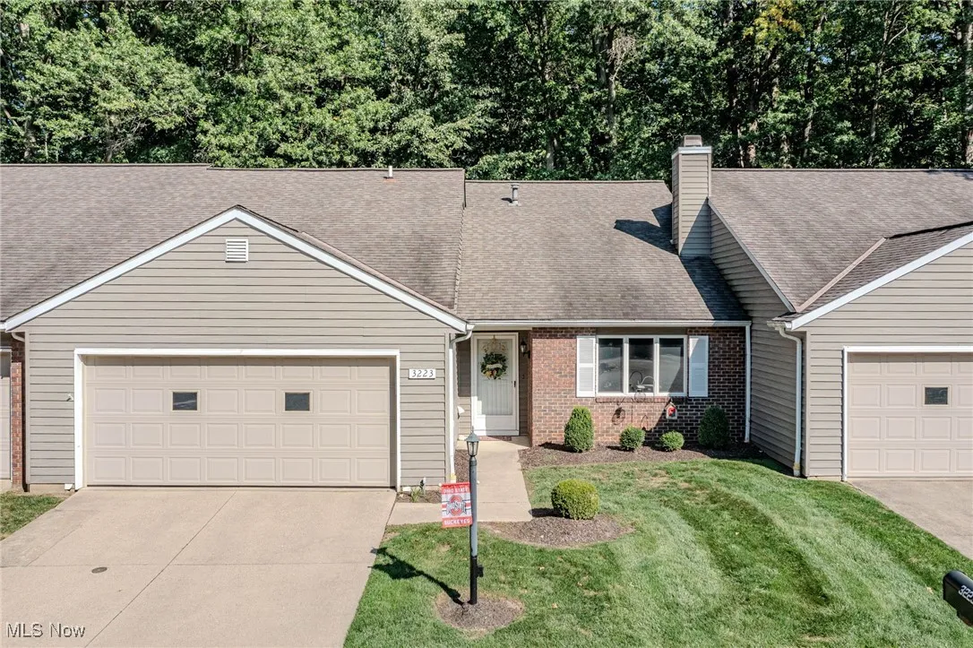 View of front of house with a shingled roof, a chimney, driveway, a front lawn, and brick siding