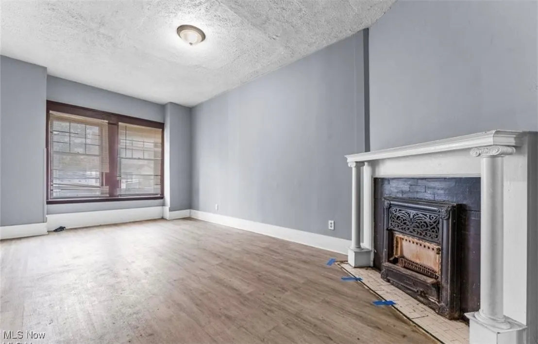 Unfurnished living room featuring a textured ceiling, light wood-style floors, and a fireplace with flush hearth