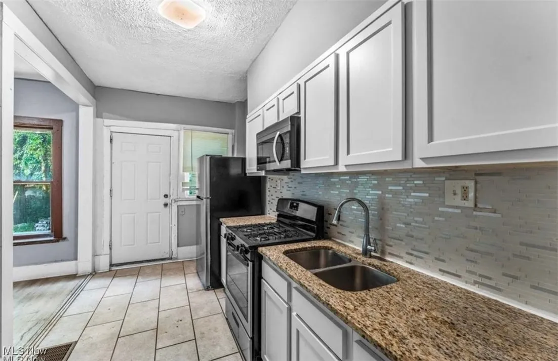 Kitchen featuring appliances with stainless steel finishes, decorative backsplash, a textured ceiling, light stone countertops, and light tile patterned floors