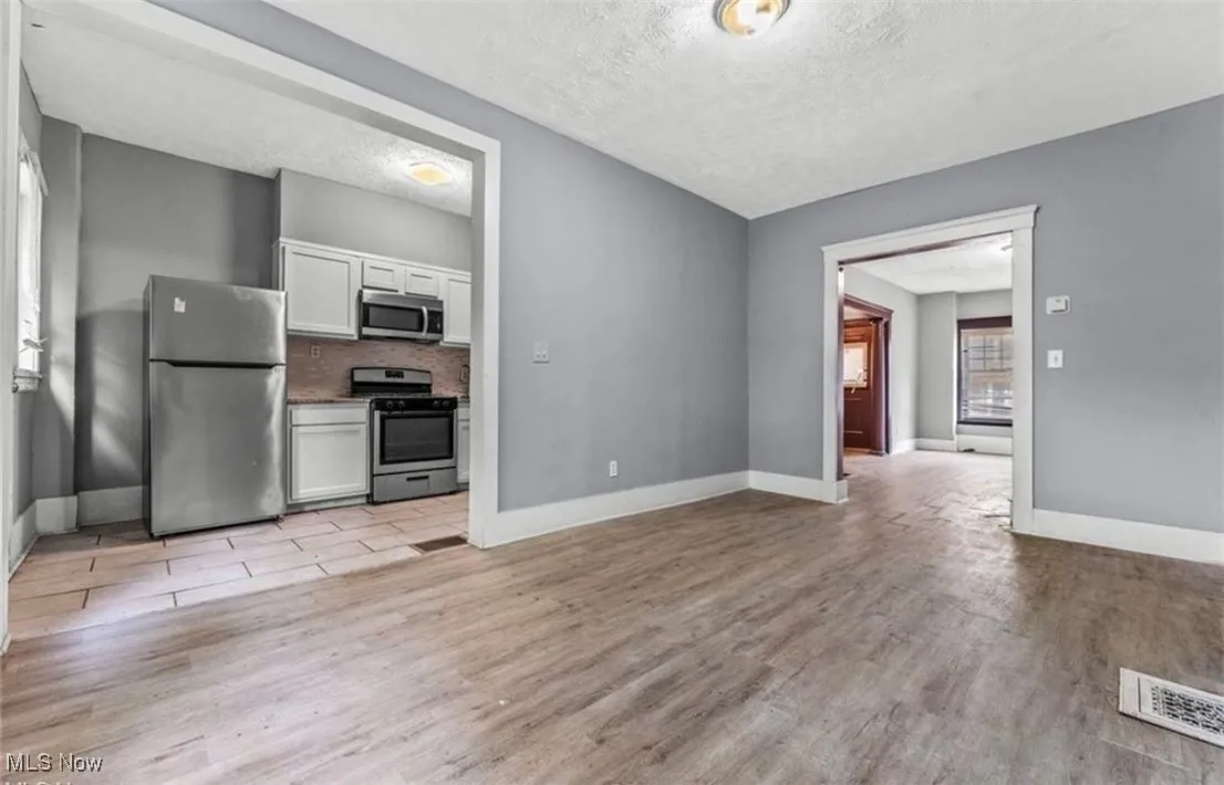 Kitchen with white cabinetry, appliances with stainless steel finishes, light wood-style floors, tasteful backsplash, and a textured ceiling