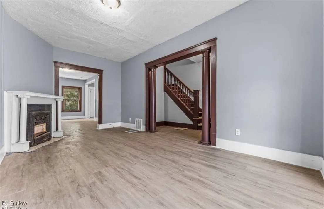 Unfurnished living room featuring light wood finished floors, a textured ceiling, stairway, a fireplace, and ornate columns