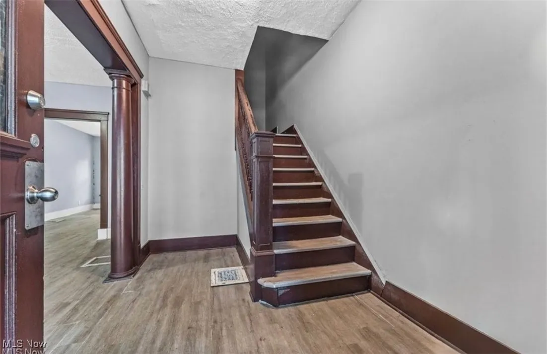 Stairway with decorative columns, wood finished floors, and a textured ceiling