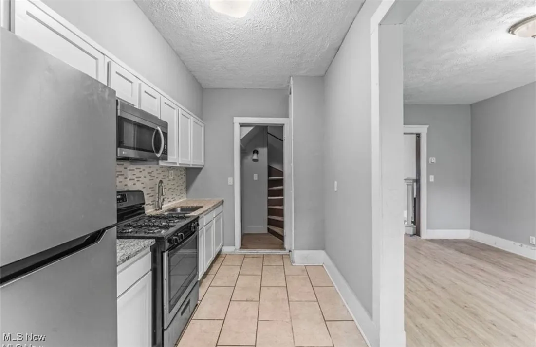 Kitchen featuring appliances with stainless steel finishes, white cabinetry, a textured ceiling, tasteful backsplash, and light tile patterned flooring