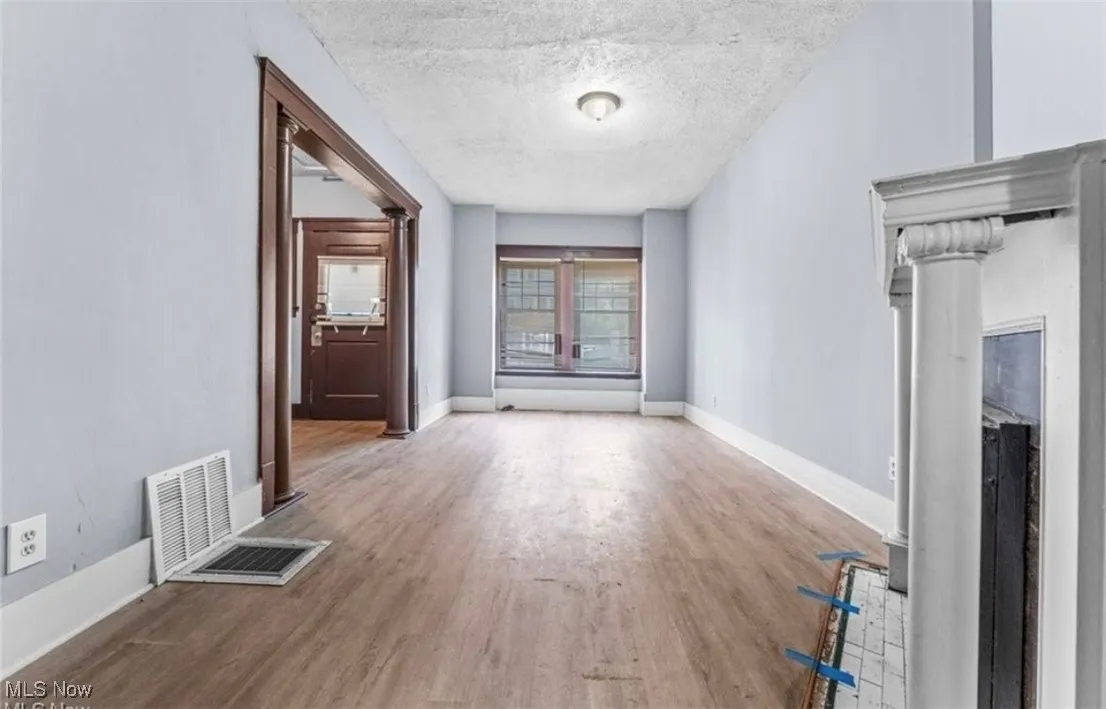 Corridor featuring a textured ceiling, light wood-style floors, and ornate columns