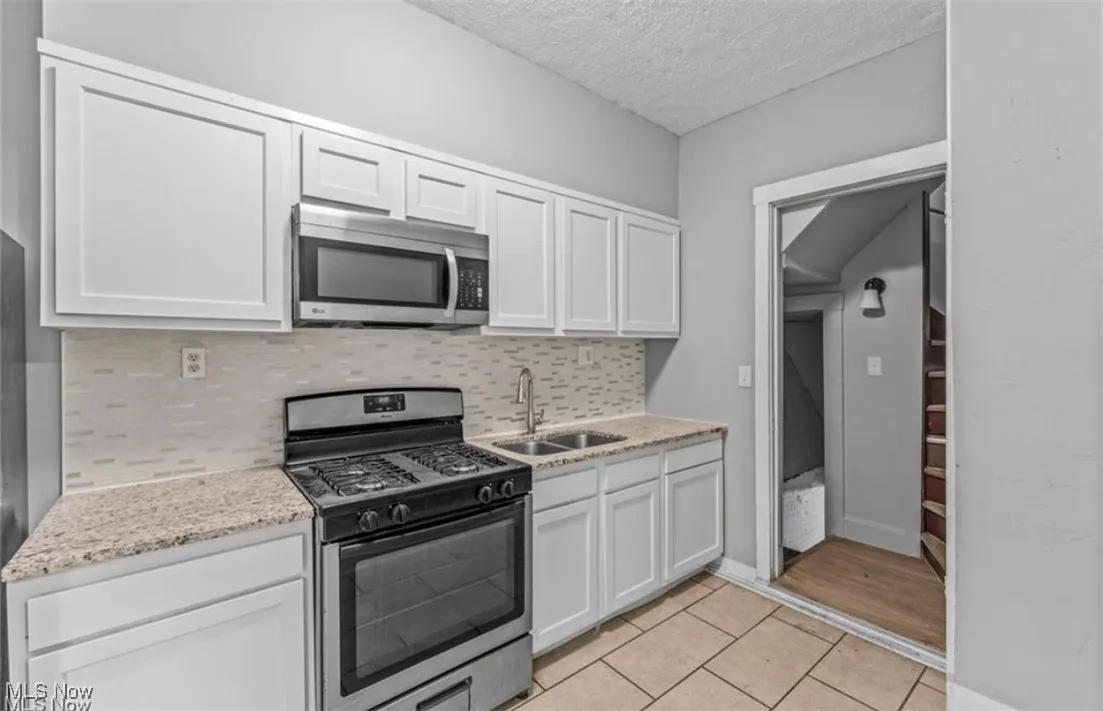 Kitchen with stainless steel appliances, light tile patterned floors, white cabinetry, tasteful backsplash, and light stone counters