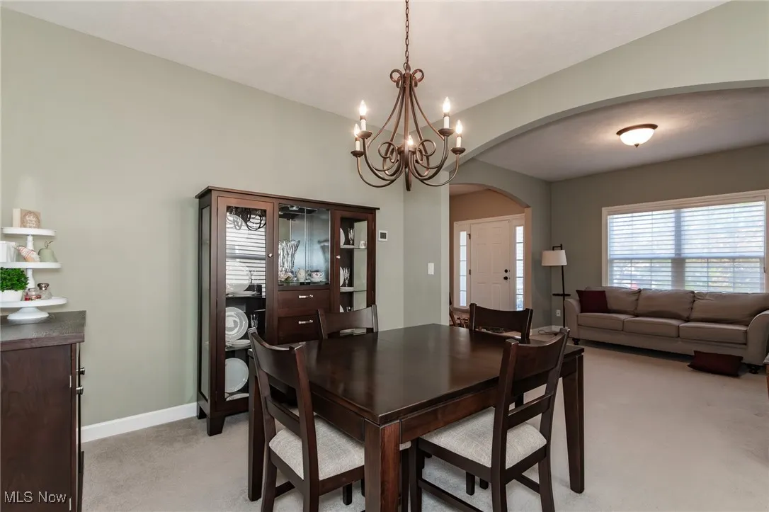 Dining room with light colored carpet, arched walkways, and a chandelier