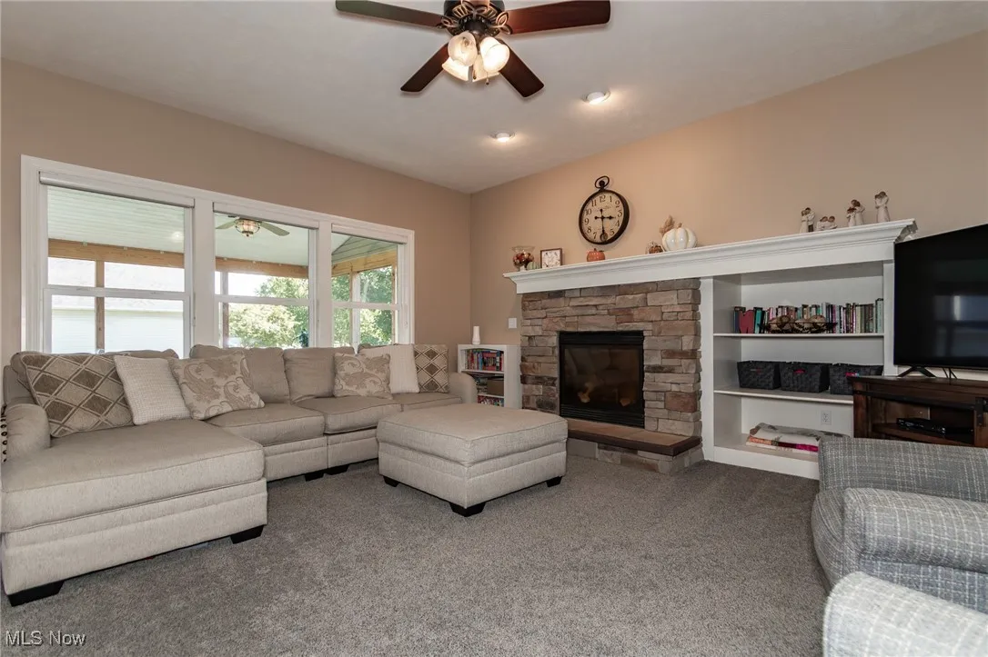 Carpeted living room featuring ceiling fan and a stone fireplace