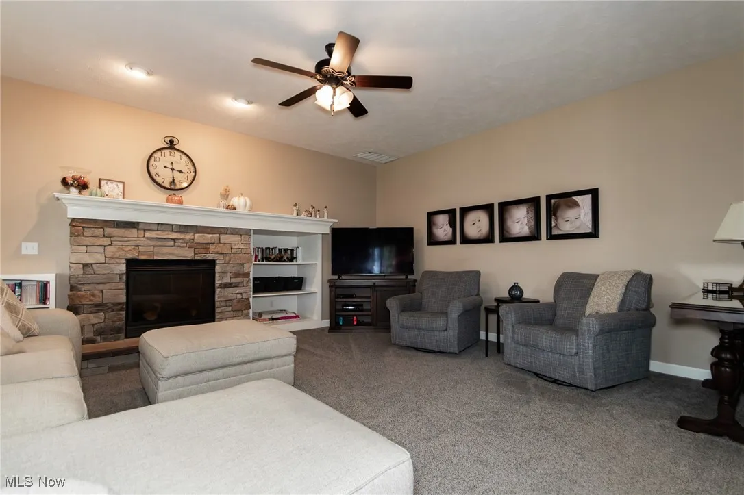 Carpeted living room with a fireplace and a ceiling fan
