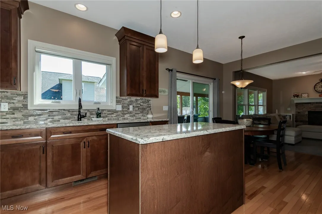 Kitchen featuring hanging light fixtures, light stone countertops, open floor plan, light wood-style floors, and a stone fireplace