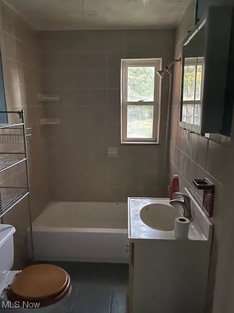 Bathroom featuring vanity, dark tile patterned floors, shower / bathtub combination, and tile walls