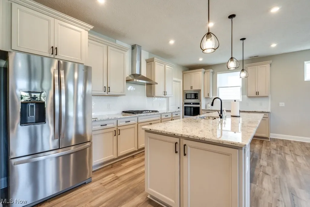 Kitchen with cream cabinetry, backsplash, stainless steel appliances, wall chimney exhaust hood, and light wood-style flooring