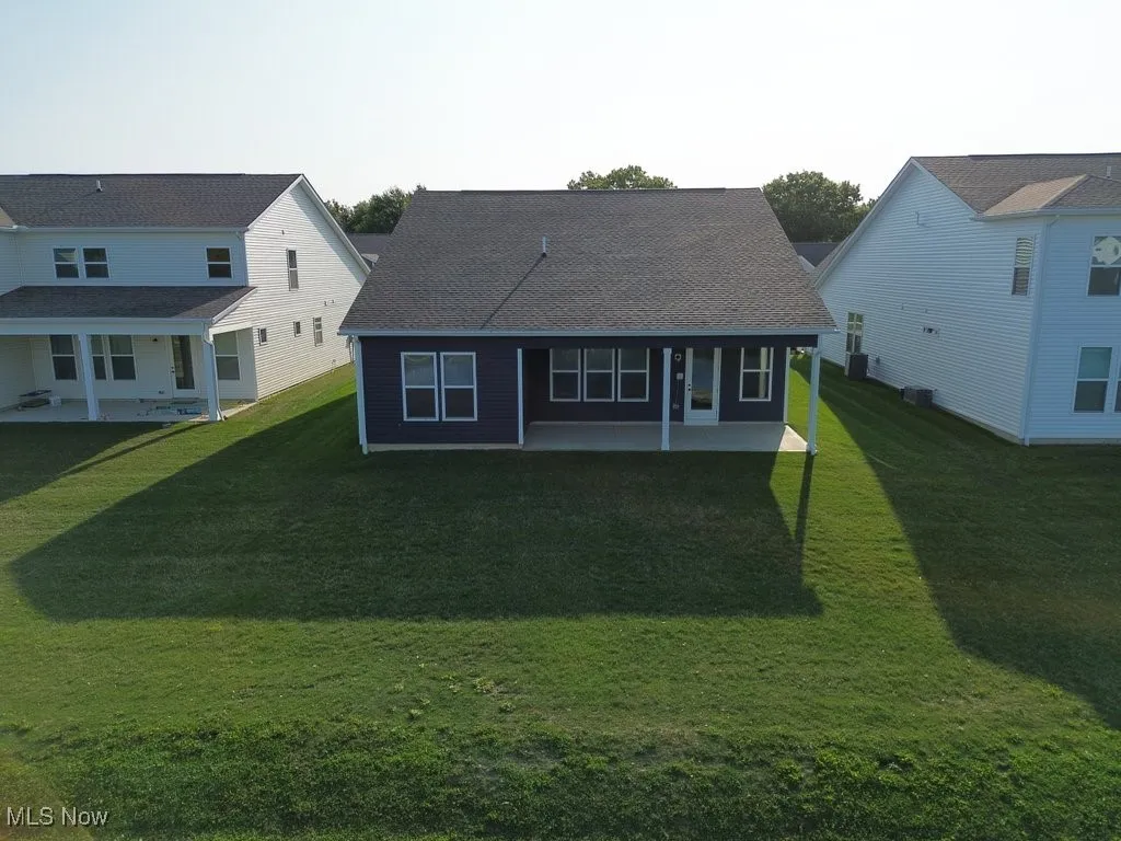 Back of house with a patio area, a lawn, and roof with shingles
