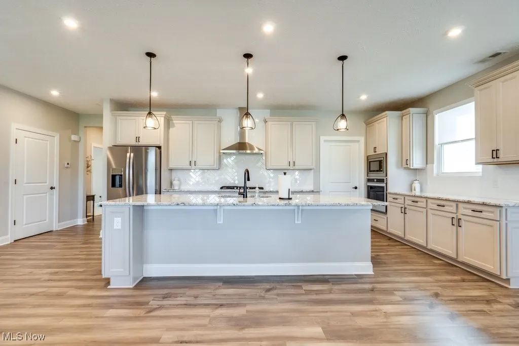 Kitchen with appliances with stainless steel finishes, pendant lighting, tasteful backsplash, light stone counters, and recessed lighting