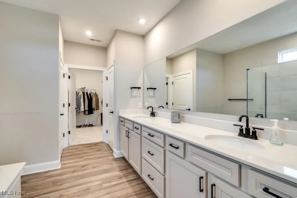 Bathroom with double vanity, a walk in closet, light wood-type flooring, a stall shower, and recessed lighting