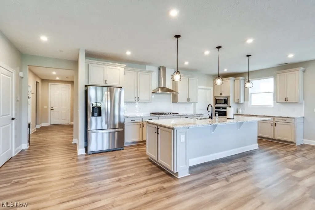 Kitchen with stainless steel appliances, decorative light fixtures, wall chimney exhaust hood, light stone countertops, and a breakfast bar