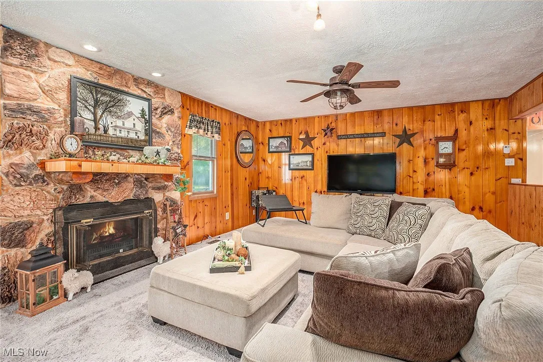 Living room featuring carpet flooring, a fireplace, wood walls, a textured ceiling, and a ceiling fan