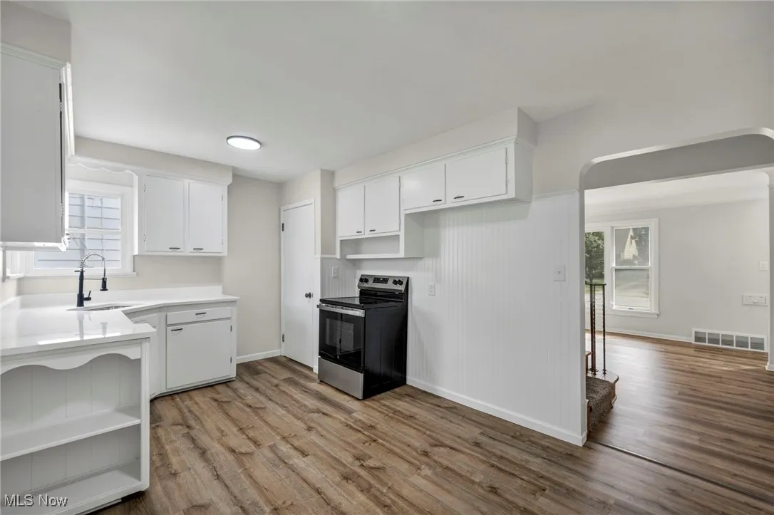 Kitchen with electric range, white cabinets, light wood-type flooring, and open shelves