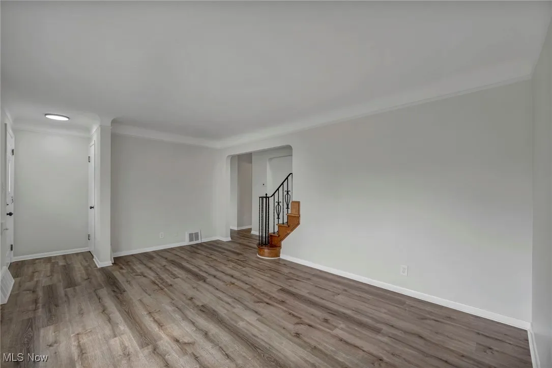 Unfurnished living room with wood finished floors, stairs, ornamental molding, and arched walkways