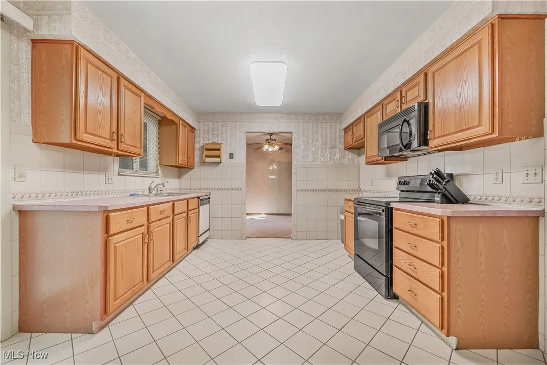 Kitchen with wallpapered walls, black appliances, light countertops, ceiling fan, and light tile patterned flooring