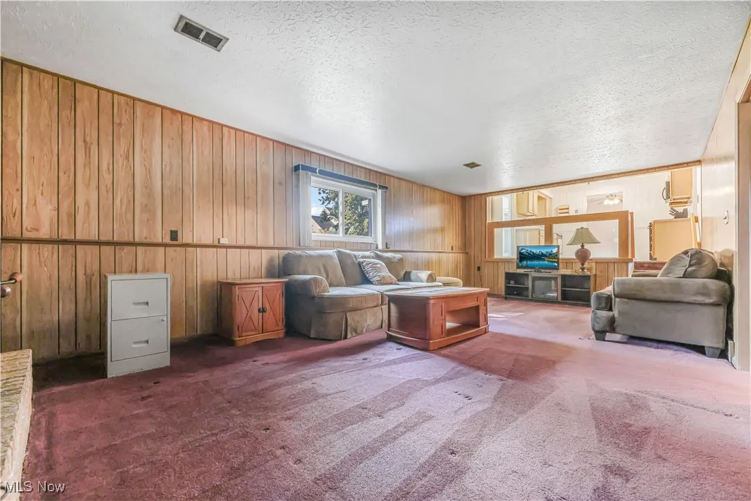 Carpeted living room featuring wood walls and a textured ceiling