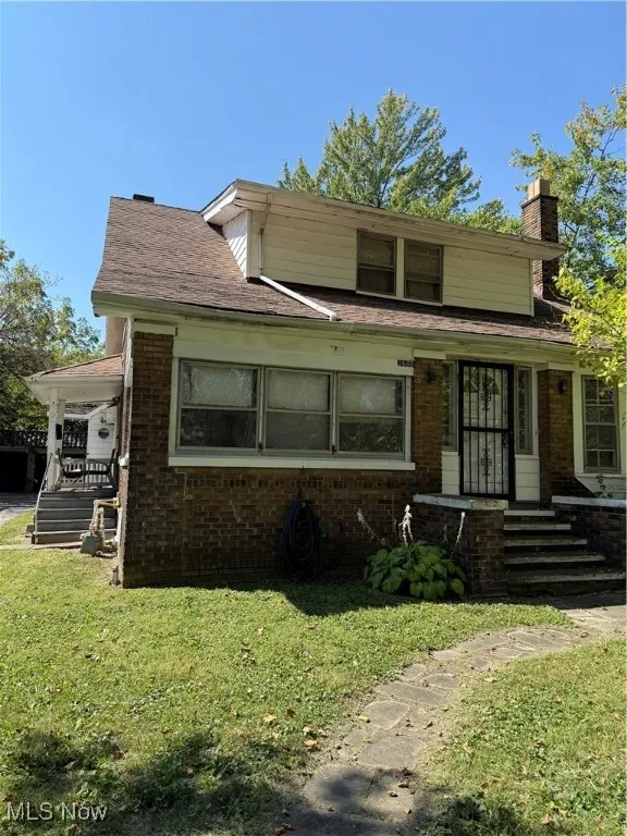 View of front of property with a chimney, brick siding, and a front lawn